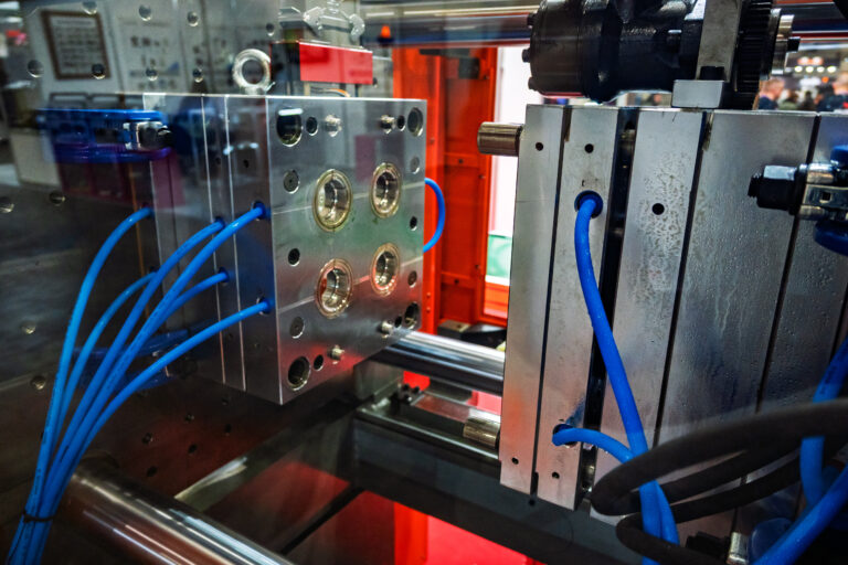 Close-up view of a shiny metal injection molding tool or die with blue hoses, part of an industrial manufacturing machine used for plastic production